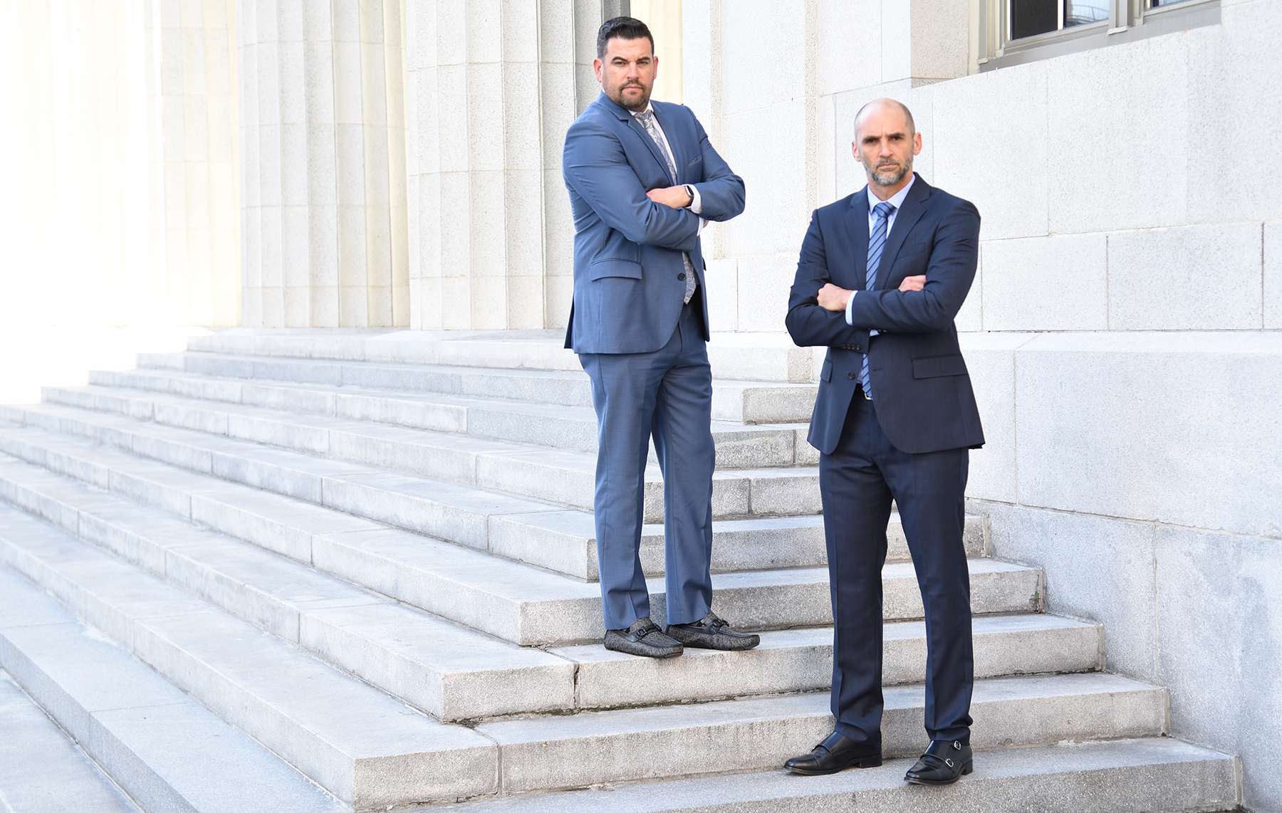 Bram J. Gechtman and Darien McMillan standing on the steps to a courthouse with their arms folded across the front of their bodies
