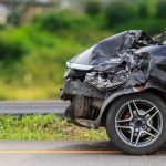 Black car on the road that has been involved in a car accident that has damaged the front of the car