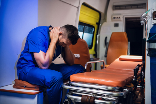 Exhausted paramedic in back of emergency vehicle sitting on a stretcher with his head down and hands around his neck