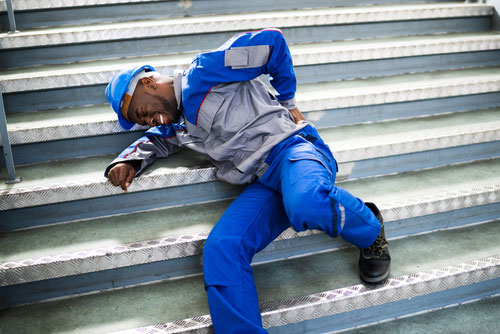 Male worker laying sideways on a set of stairs holding his back in pain