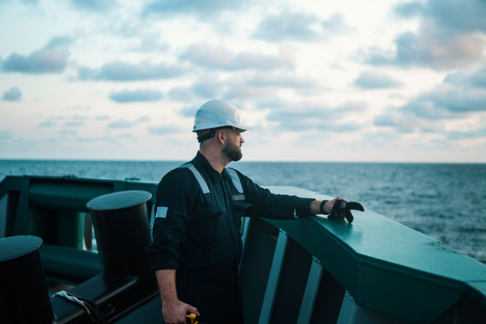 A marine deck officer standing on the deck of a ship looking out at the water