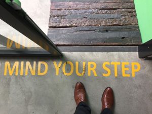 The words Mind Your Step painted on an entryway with a person's feet approaching