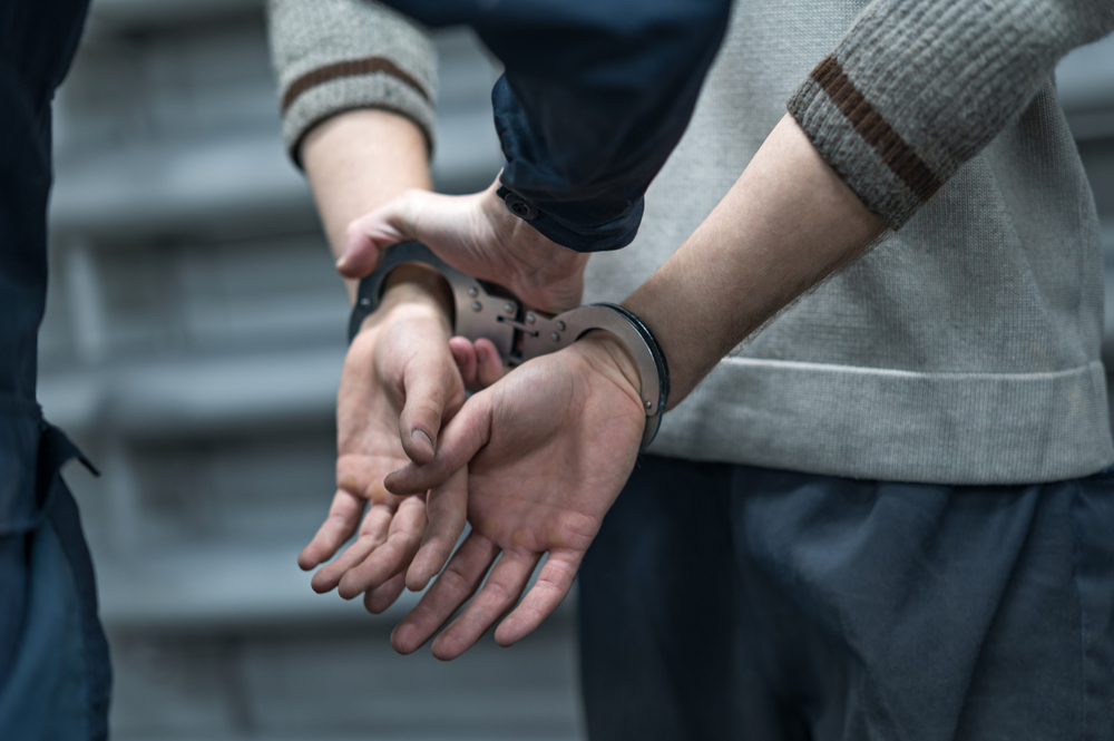 Close up of a person's hands behind their back with handcuffs on and being escorted